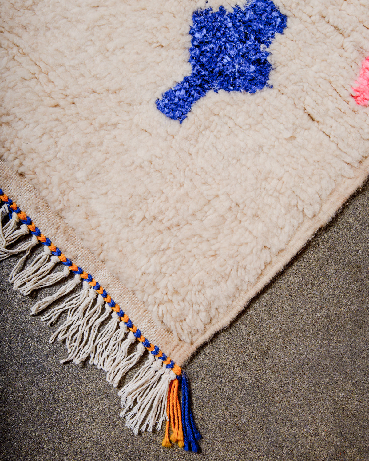Corner of cream Azilal rug with a tightly woven edge and white cotton tassels across the end.